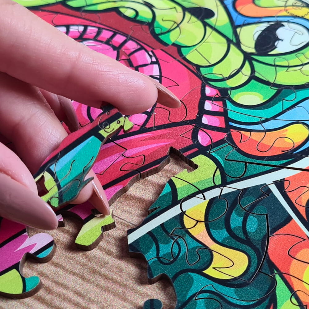 Mão segurando peça de cachorro para encaixe em quebra-cabeça de madeira da cobra.