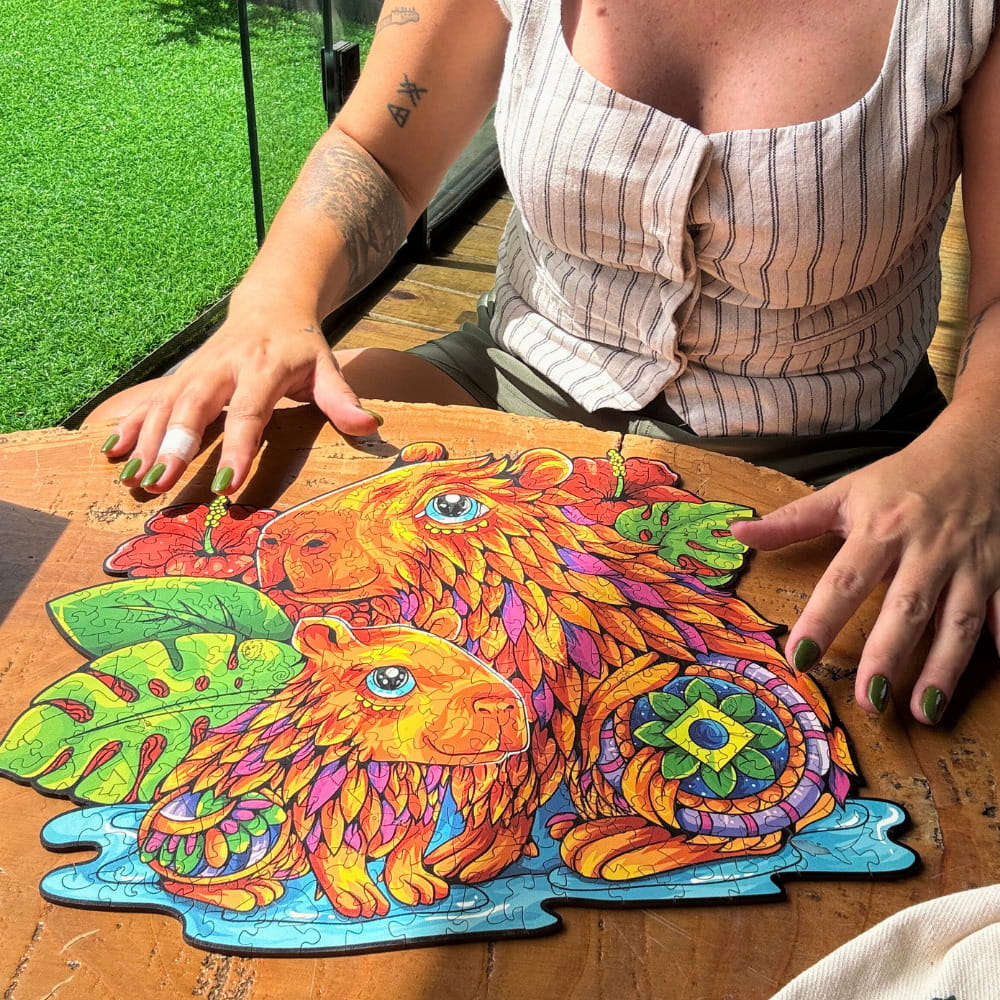 Mulher montando quebra-cabeça de madeira artesanal de capivara em ambiente iluminado.