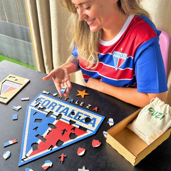 Mulher com camisa do Fortaleza Esporte Clube montando quebra-cabeça de madeira do escudo do time.