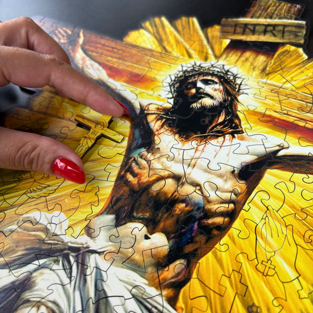 Close-up em ângulo do quebra-cabeça montado, destacando os cortes precisos da madeira. Uma mão aponta para uma peça em formato de cruz que se encaixa perfeitamente no cenário de luz radiante atrás da figura de Jesus.